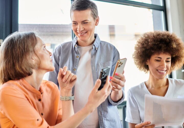 Three colleagues enjoying a casual moment with coffee and conversation at work.